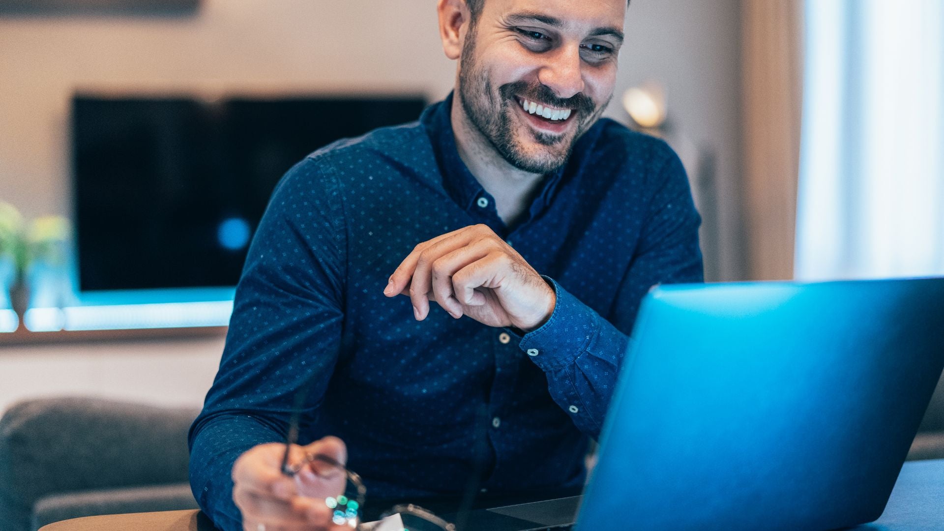 A man smiles while working on a laptop, showcasing a positive and engaged expression.